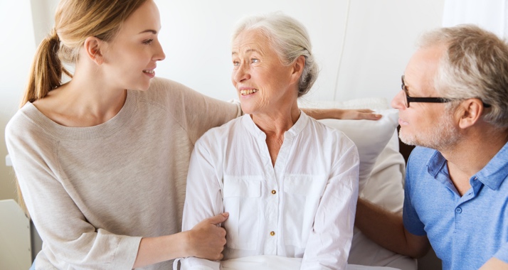 Betreuerin sitzt bei Patientin und Angehörigem auf der Couch und berät sie